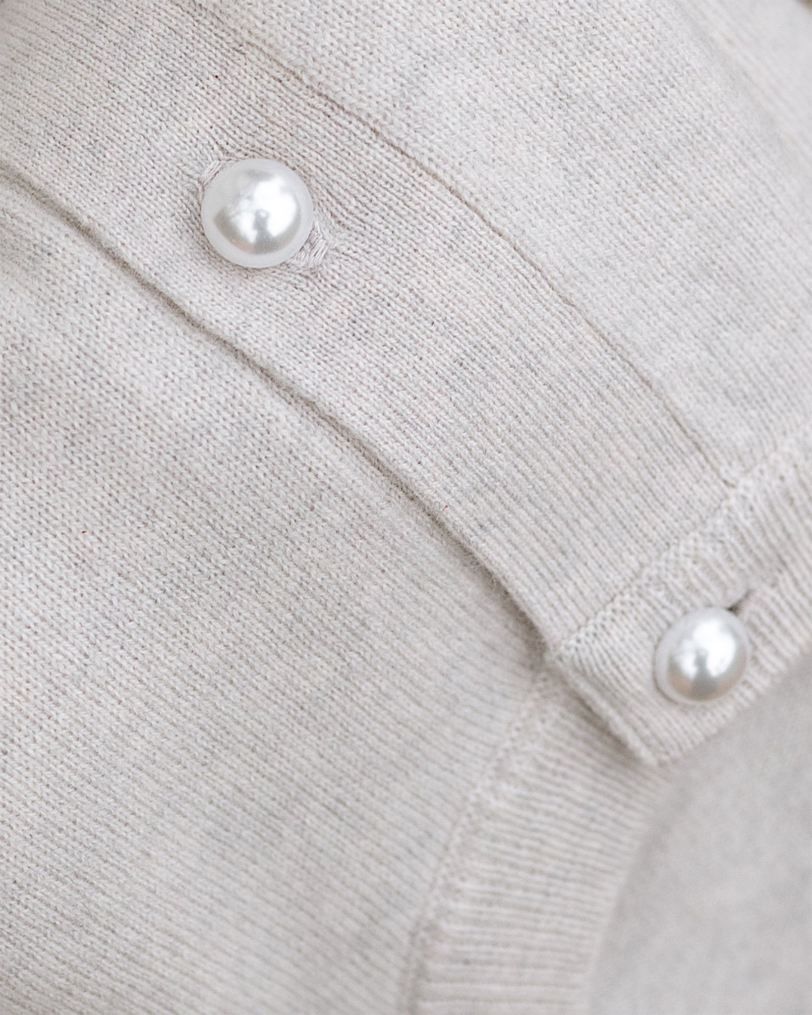 Close-up of a light gray cardigan with pearl buttons.