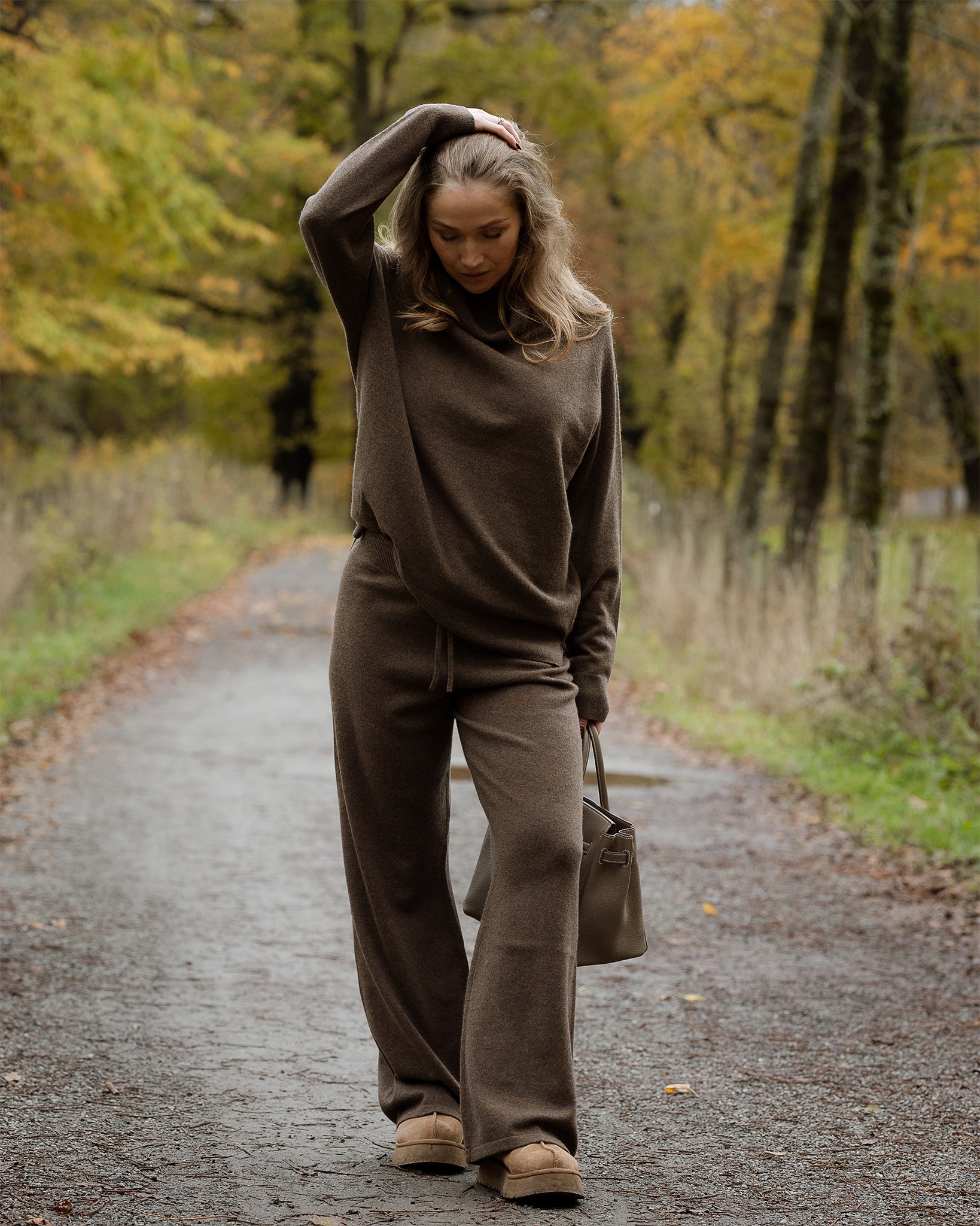 Woman in brown outfit walking on a path with autumn trees in the background