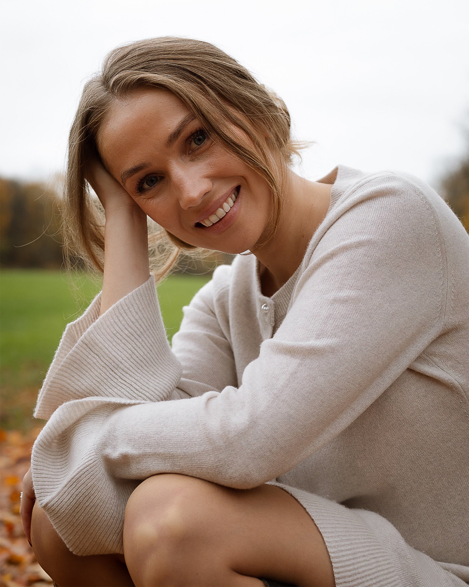Woman sitting outdoors in a natural setting, wearing a light-colored sweater.